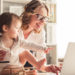 Beautiful business mom is using a laptop and smiling while spending time with her cute baby boy at home