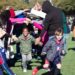 Kids in jackets and i9 Sports soccer uniforms smile and run through a tunnel formed from their parents’ outstretched arms.