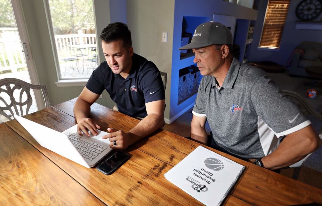 Two i9 Sports franchisees sit at a table in their home while working on a laptop.