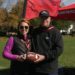 i9 Sports franchise owners Rachel and Michael DuPont hold an i9 Sports-branded football while standing in a grassy sports field by a red flag and tent.