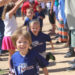 Two lines of children hold their arms overhead to form a tunnel while other children in i9 Sports jerseys run through it toward the camera.