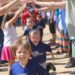 Children run beneath a tunnel formed by the upraised arms of two rows of older people.