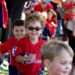 ALT: Three little boys in i9 Sports jerseys run onto a field, smiling toward the camera, with the boy in the middle wearing Wayfarer-style sunglasses.