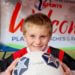 A boy holding a soccer ball in front of him smiles at the camera.