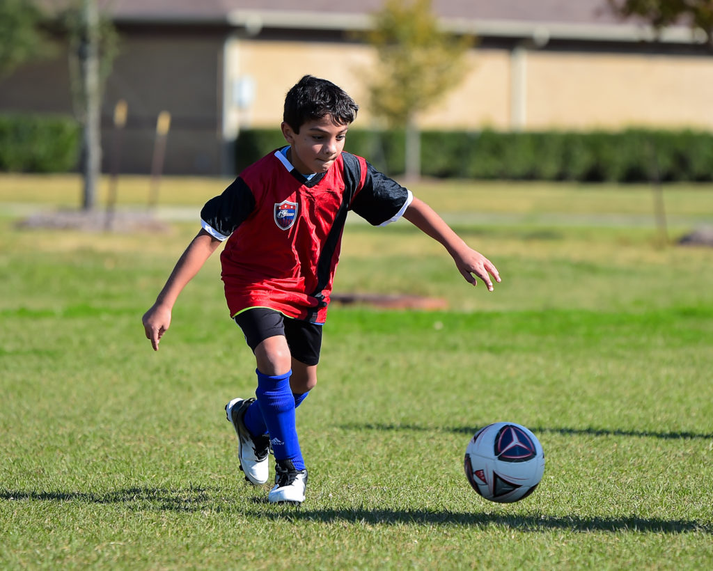 A boy runs a soccer ball across a grassy field