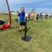 Kids in black shorts and blue i9 Sports jerseys practice their skills at socially-distant T-ball stations backed by netting.