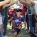 Smiling kids in i9 Sports jerseys run beneath a tunnel of hands raised overhead by adults.