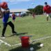 A coach in a mask pitched to a boy in an i9 Sports jersey with a bat.