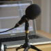 A microphone on a stand next to a pair of headphones. A slightly out-of-focus laptop is in the background. Photo credit: Nicolas Solop/Flickr Creative Commons