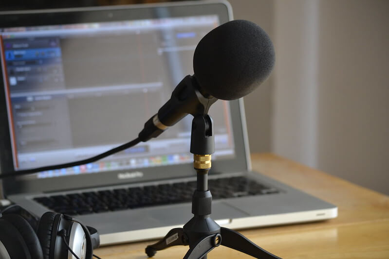 A microphone on a stand next to a pair of headphones. A slightly out-of-focus laptop is in the background. Photo credit: Nicolas Solop/Flickr Creative Commons