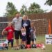 A couple and their 3 children pose in front of a net and sports equipment.