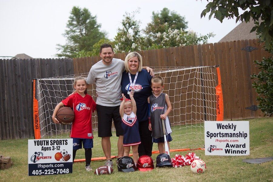 A couple and their 3 children pose in front of a net and sports equipment.