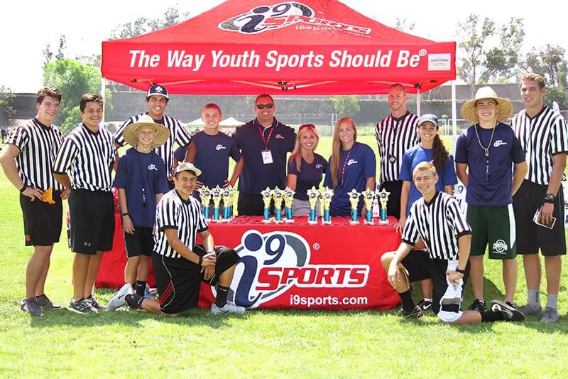 i9 Staff, referees, and coaches stand at a portable gazebo tent