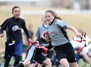 A girl races upfield with the football as other kids pursue her during a game of flag football.