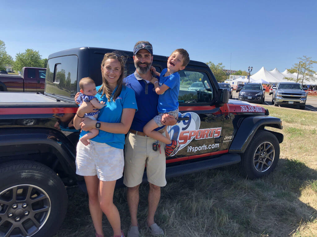 From left: 2-month-old Harper rests in the arms of her mom, Amy, while Janson Kinsley holds the couple's older son, Carter. The family is standing in front of their Jeep Gladiator pickup truck, which is decorated with the i9 Sports red white and blue logo and color scheme.