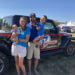 From left: 2-month-old Harper rests in the arms of her mom, Amy, while Janson Kinsley holds the couple's older son, Carter. The family is standing in front of their Jeep Gladiator pickup truck, which is decorated with the i9 Sports red white and blue logo and color scheme.
