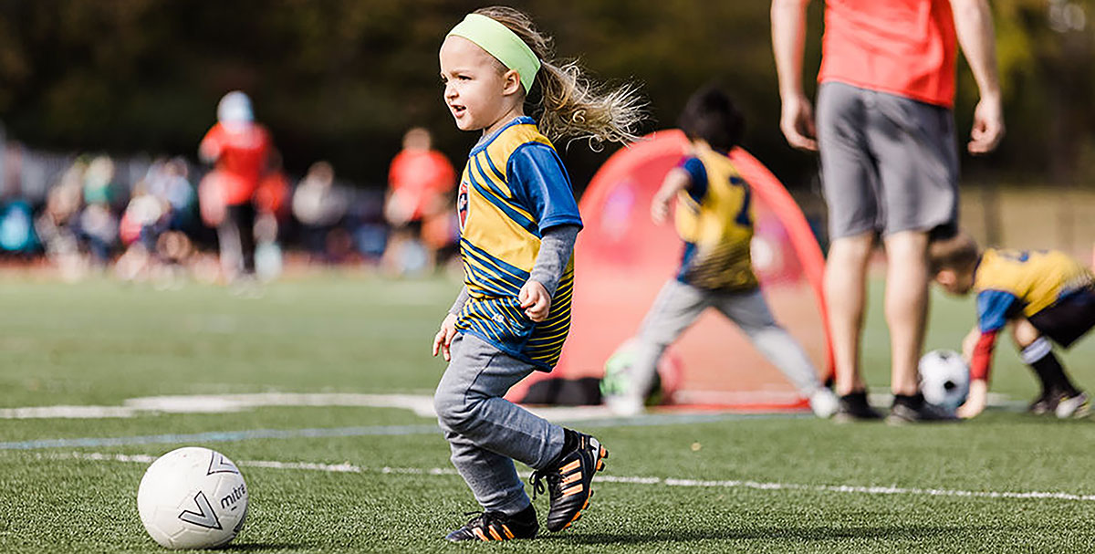 A small girl chases a soccer ball.