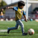 A little boy is running to kick a soccer ball.