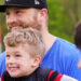 A boy smiles as he watches a game while sitting in his dad's lap. i9 Sports is one of the best franchises to own.