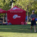 Man walks across a field carrying equipment. i9 Sports tents are in the background.